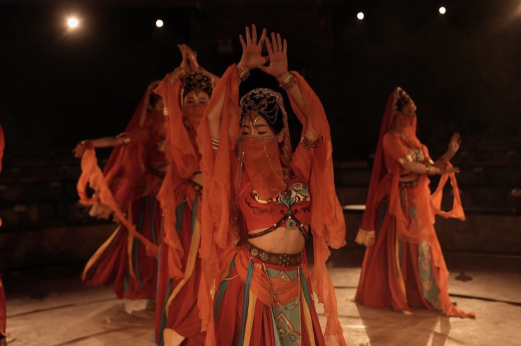 Dancers in amber robes, arms raised