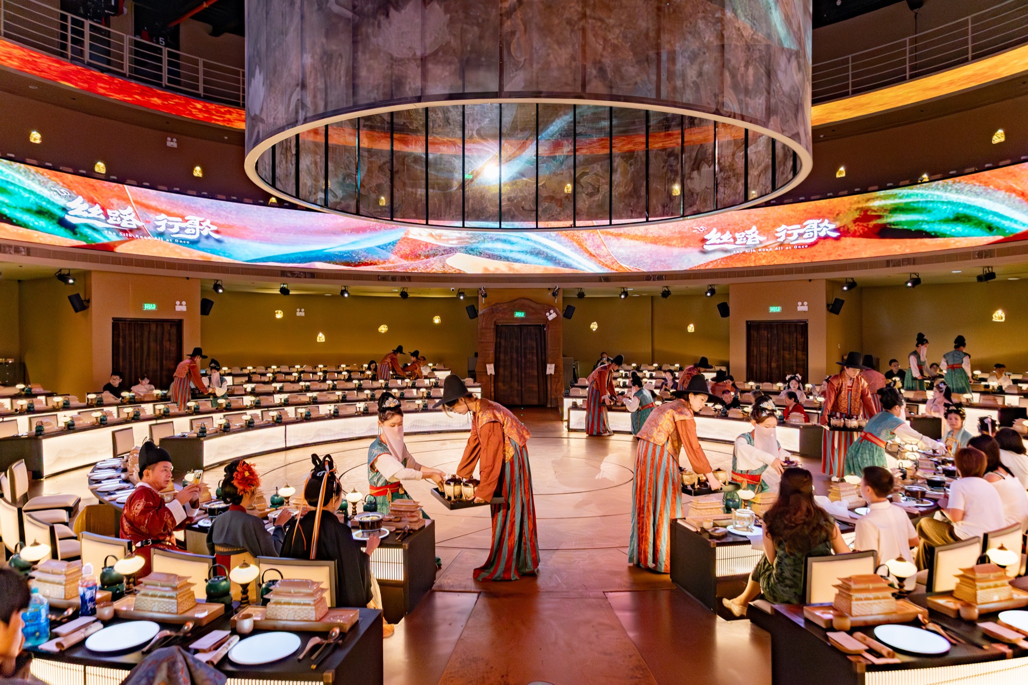 Performers circling the round stage beneath warm light