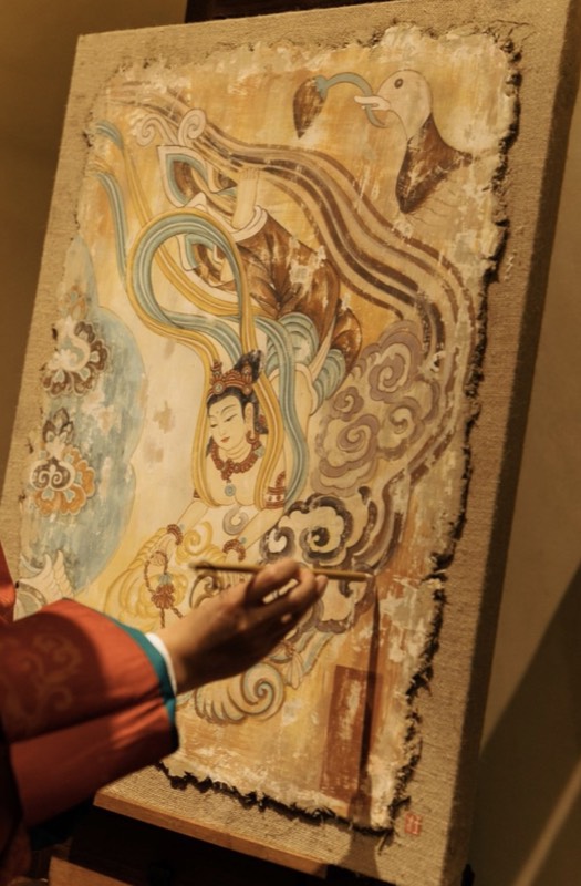 An artist painting a Dunhuang mural with mineral pigments